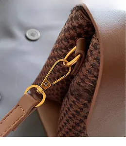 Close-up of golden metal hook on brown woven and leather crossbody bag detail