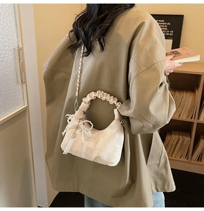 Detail of cream pleated handbag with pearl lace bow charm and metal chain strap