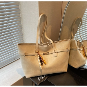 Detail of a large cream tote bag with metal buckle and colorful wooden bead keychain