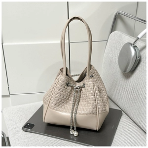 Detail of woven bucket bag featuring elegant pearl drawstring and metallic chain accents