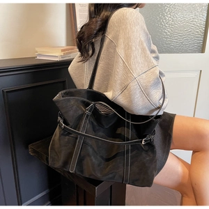 Detail view of large black tote bag with white contrast stitching and buckle straps