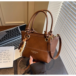 Close-up of brown bucket bag with beaded charm and logo print on desk