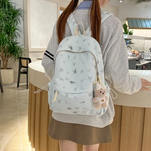 Detail of light blue nylon student backpack featuring butterfly patterns and a plush bear charm