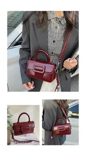 Detail view of burgundy glossy leather square handbag with top handle and metal buckle strap