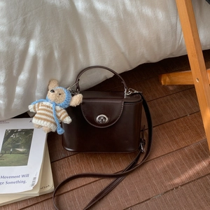 Close-up of a dark brown box crossbody bag with a cute teddy bear charm and silver twist lock