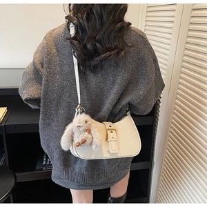 Detail of white crescent shoulder bag featuring a gold buckle and cute rabbit plush charm