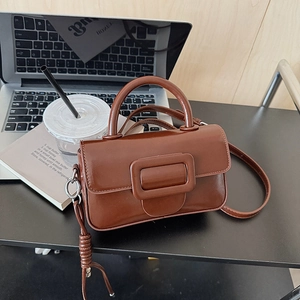 Detail shot of the caramel brown leather handbag with a large gold buckle on a desk