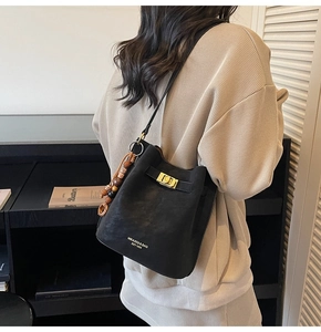 Detail view of black matte bucket bag featuring vintage bead charm and gold lock buckle