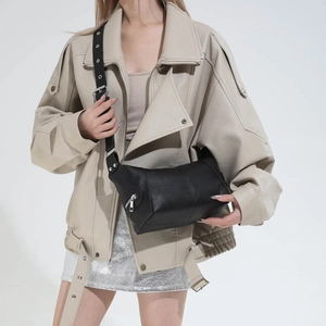Detail of a black leather underarm bag with adjustable strap and silver metal eyelets