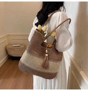 Detail of woven straw tote bag with gradient stripes and decorative wooden bead tassels