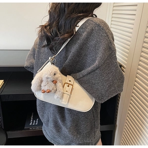 Detail of cream white leather hobo bag with gold buckle and plush rabbit charm