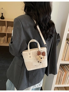 Sac seau tissé beige élégant avec pendentif ours, porté par un mannequin en intérieur