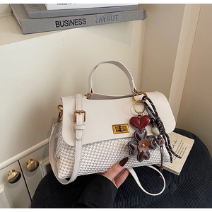 Detail view of woven tweed and white leather handbag with golden lock and flower charm