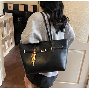 Detail of black PU leather tote bag featuring a silver metal lock and beaded charm