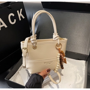 Detail of cream white leather bucket bag with decorative beaded charm and gold hardware
