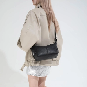 Detail of black dumpling bag in litchi grain leather with silver zipper on model
