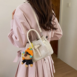 Detail der beigen Eimertasche mit süßem orangem Hundeanhänger und Lederriemendekor