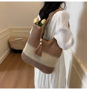 Detail view of woven straw tote bag with striped pattern and decorative tassel charm