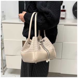 Detail of cream beige woven bucket bag with silver chain and pearl charms on a model