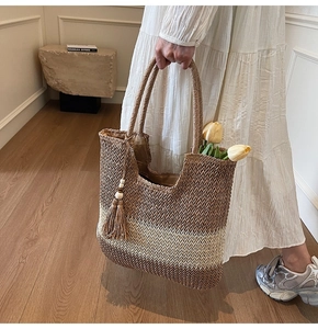 Detail of woven straw tote bag with gradient stripes and decorative wooden bead tassels