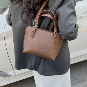 Street style shot of a brown bucket bag with lychee grain texture and silver buckles