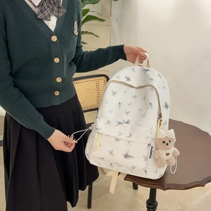 Close-up of white nylon school backpack featuring grey butterfly patterns and a cute bear charm
