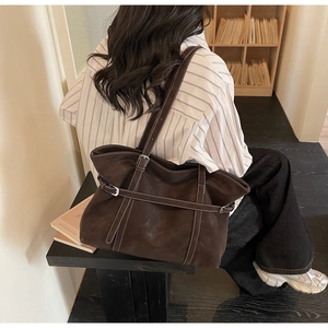 Detail view of coffee suede tote bag with contrast stitching and metal buckle on long strap