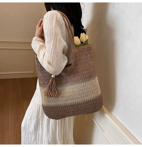 Macro detail of hand-woven straw tote bag showing brown striped texture and tassel