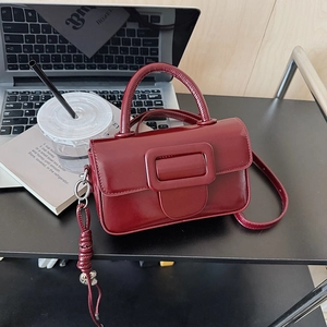 Detail of burgundy glossy leather handbag with square buckle in a modern office setting