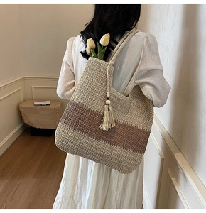 Detail of hand-woven beige and brown tote bag with decorative fringe on model's shoulder