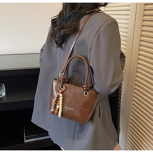 Brown leather bucket bag with top handles and beaded charm shown on a female model