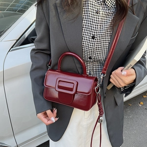 Detail shot of a dark red patent leather handbag featuring a glossy finish and top handle