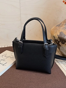 Minimalist black lychee leather bucket bag with silver buckles on a brown fabric surface