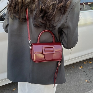 Outdoor shot of a wine red patent leather handbag with large square buckle shown on a model