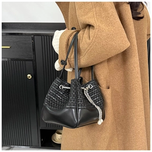 Detail of black woven bucket bag with drawstring closure and elegant silver pearl chain strap