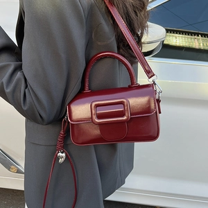 Deep red square crossbody bag detail featuring a large decorative buckle and heart pendant