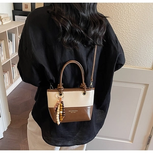 Close-up of dual-tone leather bucket bag with wooden bead charm and gold lettering