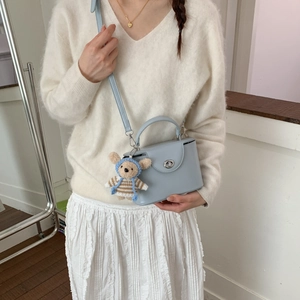 Detail of light blue crossbody box bag with silver twist lock and cute teddy bear charm