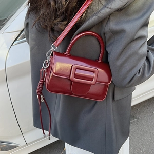 Detail of burgundy patent leather handbag with stylish rectangular buckle on a grey suit