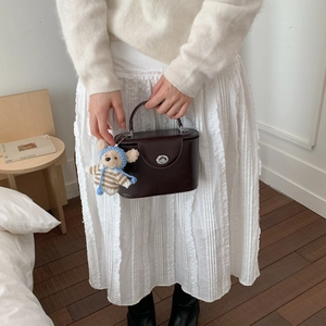 Detailed view of dark brown leather crossbody bag with silver twist lock and bear charm