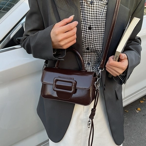 Detail of dark chocolate square handbag with leather buckle worn with a grey blazer