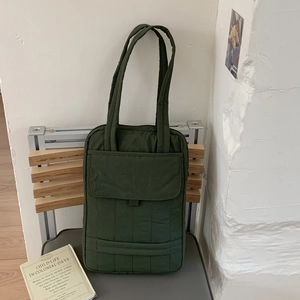 Detail of dark green quilted tote bag with front flap pocket on a wooden chair