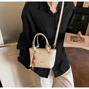 Close-up of cream crossbody bucket bag with beaded tassel detail and leather texture