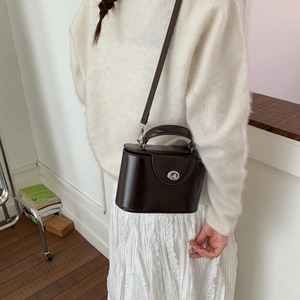 Detail of a dark brown vintage box bag styled on a model with a silver clasp and leather finish