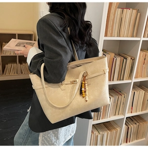 Detail of beige textured leather tote bag featuring a decorative beaded charm and metal clasp