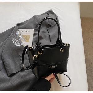 Detail of black bucket bag with gold hardware and dual handles on casual outfit
