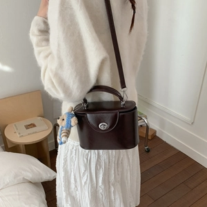 Detail of vintage brown leather box bag with metal handle and cute teddy bear charm