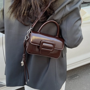 Detail view of dark coffee leather handbag featuring a large square buckle and metallic pendant