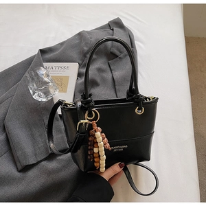 Close-up of black leather bucket bag with gold rings and colorful beaded charm detail