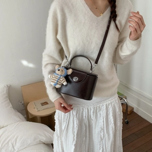 Detail of dark brown leather crossbody bag with a cute teddy bear charm on the strap